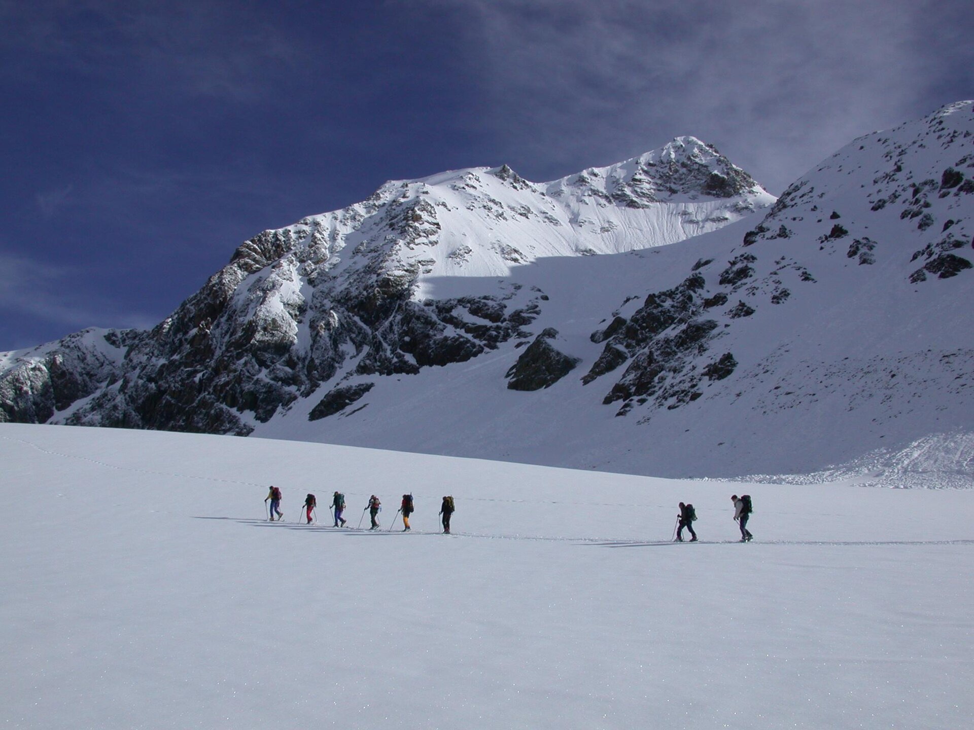 A line of ski tourers crossing a glacier below a peak